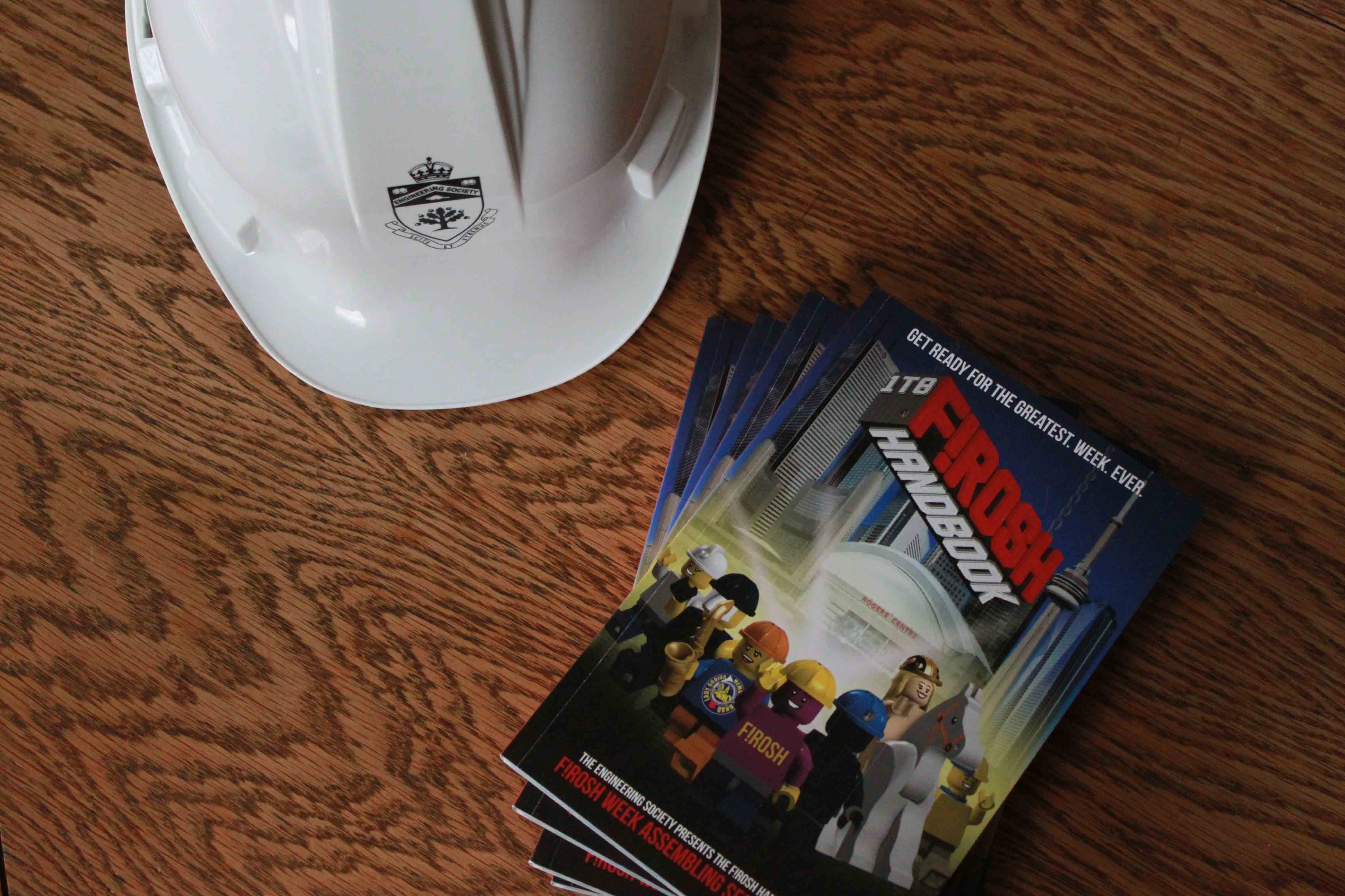 A stack of Frosh Handbooks next to a white hardhat on a wooden table