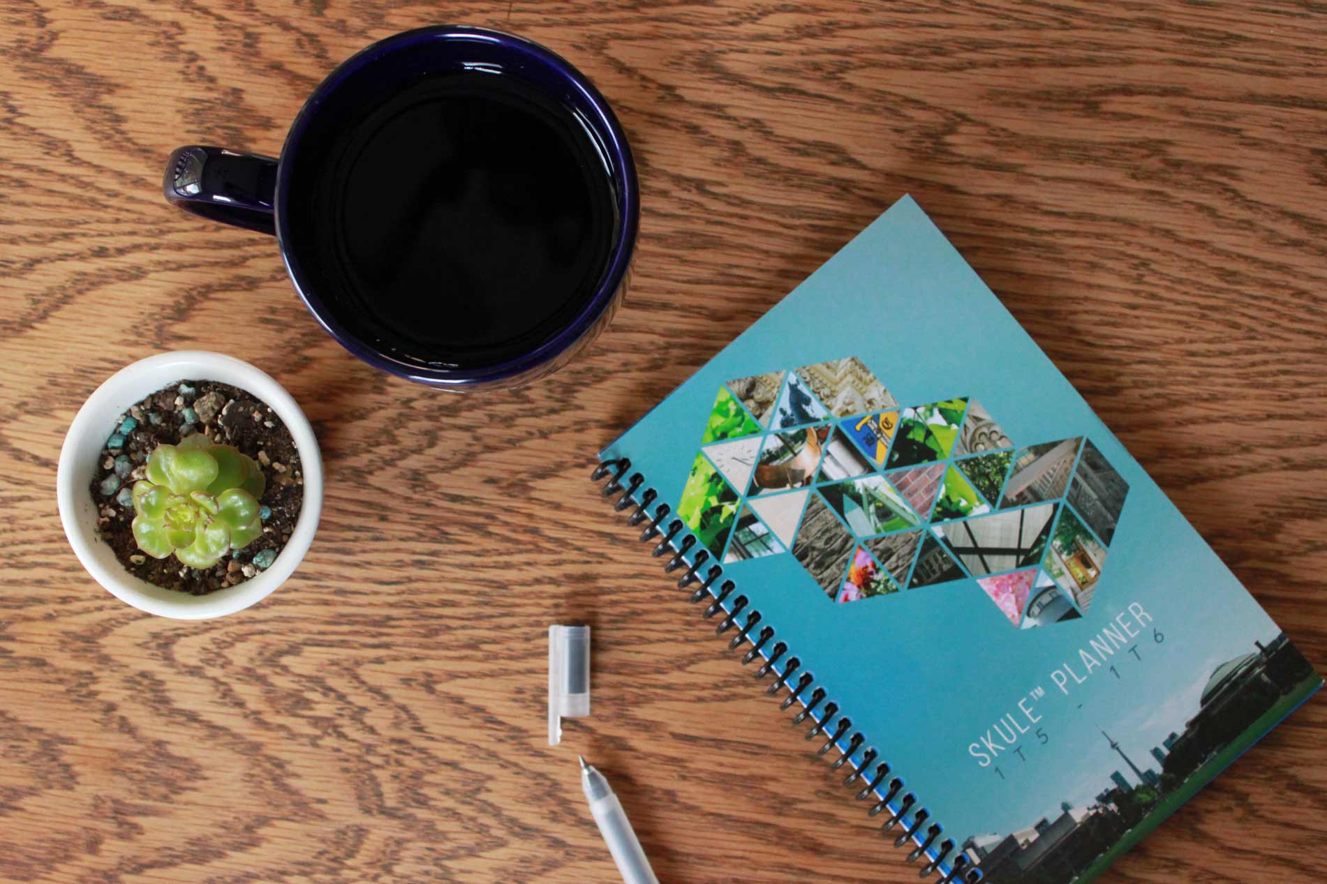 Skule Planner laid on a wooden table alongside a mug, pen, and plant