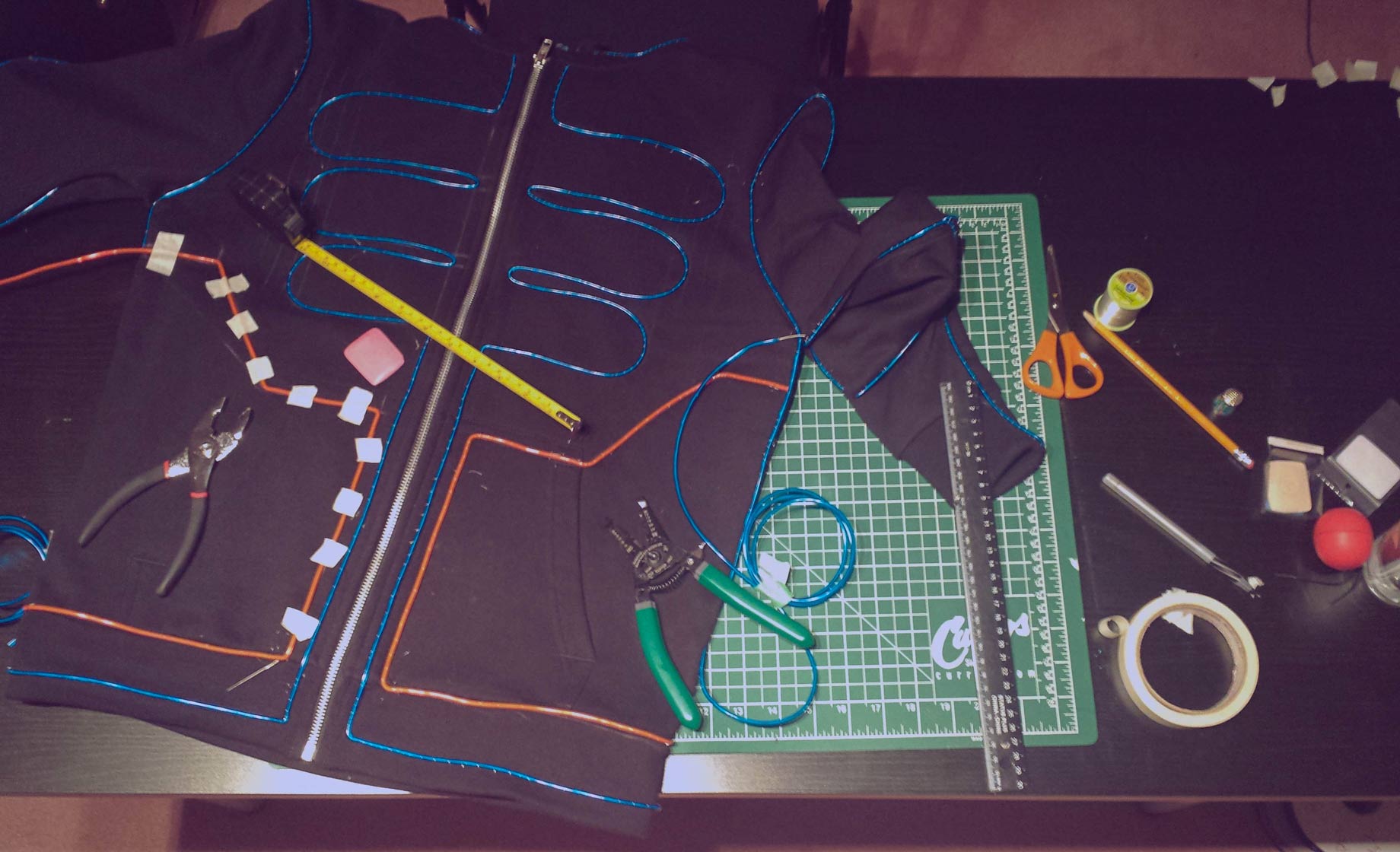 Progress photo showing the costume hoodie laid out on a table with tape, chalk, pliers, and a ruler